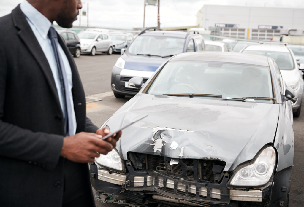 Male Insurance Loss Adjuster With Digital Tablet Inspecting Damage To Car From Motor Accident